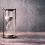 A classic hourglass with sand on a rustic wooden table against a soft gray background, offering ample copy space.